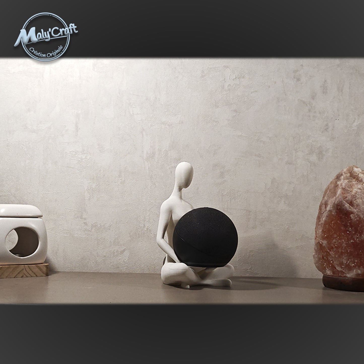 Support Echo Dot imprimé en 3D, figurine minimaliste assise en lotus, posé sur un meuble entre une lampe de sel et un diffuseur. Design zen et moderne, fabriqué en France. 3D printed Echo Dot stand, minimalist figurine in lotus pose, placed on a shelf between a salt lamp and an oil burner. Zen and modern design, handmade in France.