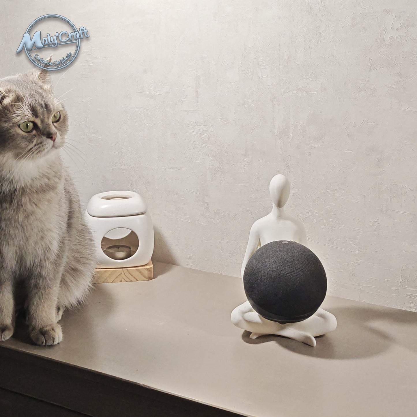Support Echo Dot imprimé en 3D en forme de figurine lotus, posé sur un meuble aux côtés d’un chat gris. Design minimaliste et zen, fabriqué en France.
3D printed Echo Dot stand shaped as a lotus pose figurine, placed on a shelf next to a grey cat. Minimalist and zen design, handmade in France.