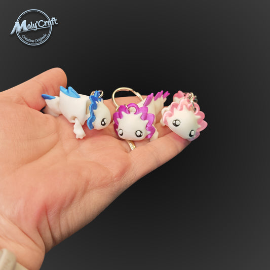 Trois porte-clés axolotls articulés suspendus, montrant les variantes de couleurs bleu, rose et vert pastel avec une finition mate.