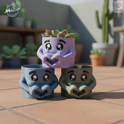 Trois petits cache-pots en forme de personnages tenant un cœur avec leurs mains, imprimés en 3D par Maly’Craft en PLA coloré (bleu, vert et lavande). Design mignon et original, idéal pour plantes grasses ou succulentes. Photo prise en extérieur sur une terrasse avec d'autres pots en arrière-plan.