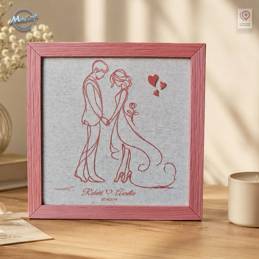 Cadre de mariage personnalisé rose posé sur une console en bois, avec dessin du couple imprimé en 3D directement sur lin, prénoms et date personnalisés, dans un décor romantique aux tons naturels.
Personalized pink wedding frame displayed on a wooden console, featuring a couple line drawing 3D printed directly onto linen with custom names and date, styled in a soft romantic natural setting.