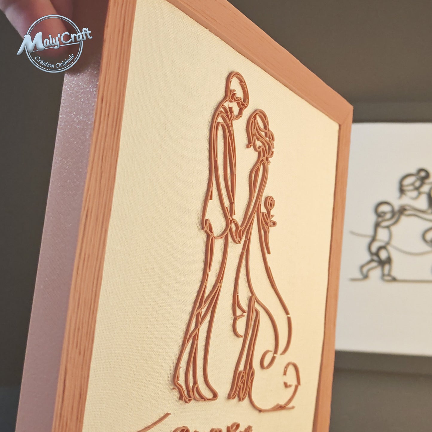 Vue rapprochée du cadre mariage Maly’Craft. Couple filaire imprimé en 3D couleur terracotta sur tissu blanc, alliance d’élégance et de douceur pour une déco artisanale.