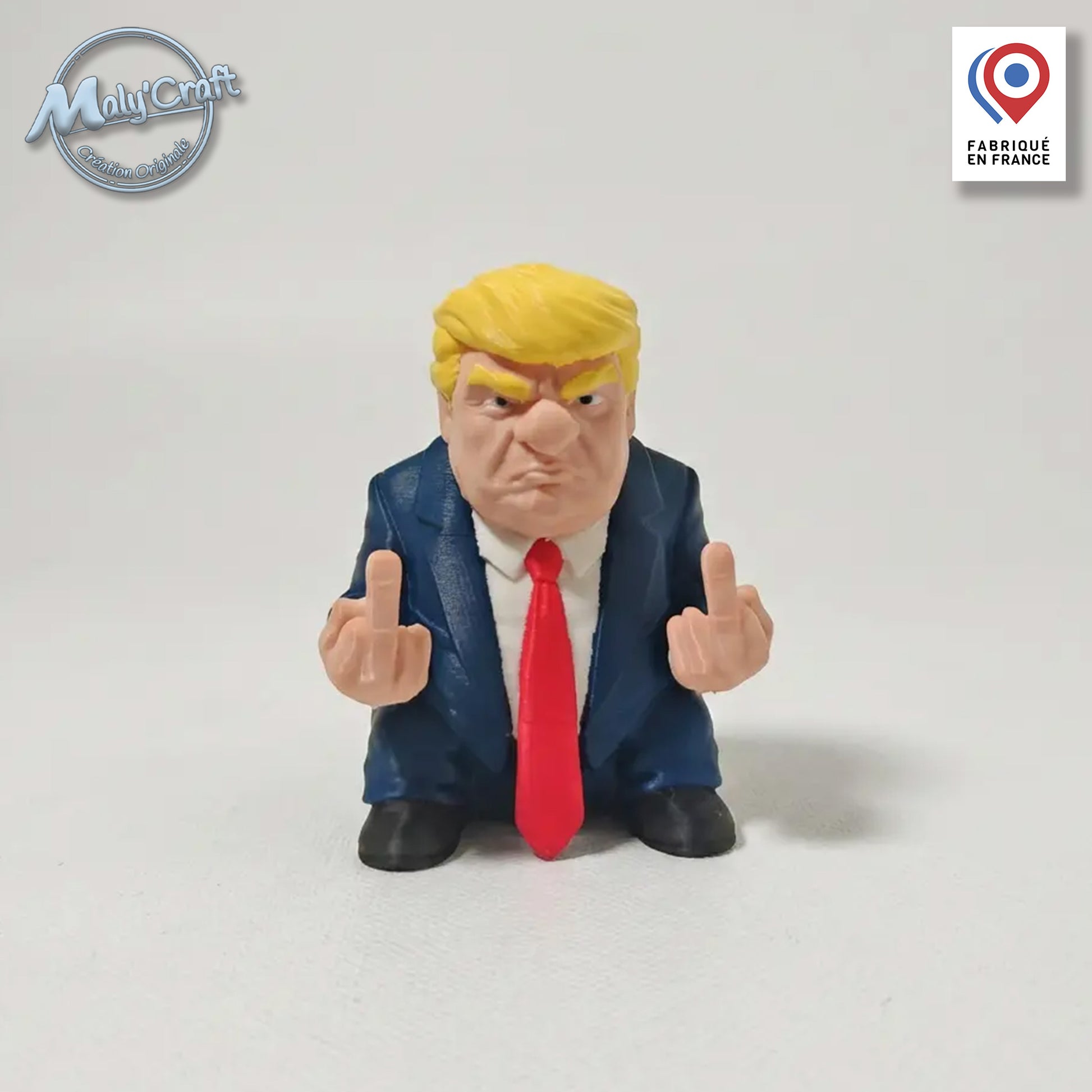 Figurine de Donald Trump en costume bleu et cravate rouge faisant un double doigt d'honneur, impression 3D de précision sur fond blanc uni. La finition est précise et qualitative grâce à l'usage de filaments de marques premium (Panchroma, Polymaker, Sunlu, Bambulab...)