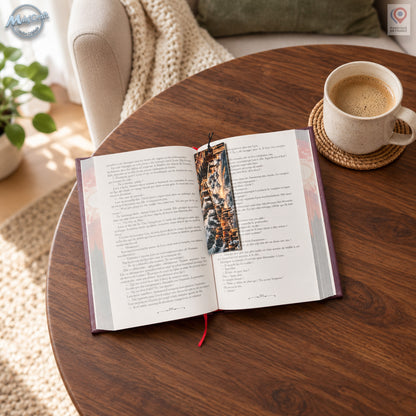 Marque-page dragon posé sur la page droite d’un roman ouvert, près de la reliure. Son illustration fantasy sombre et dorée se détache des pages claires, avec un petit cordon noir dépassant au-dessus. Le livre repose sur une table en bois, près d’une tasse en céramique. Un fauteuil beige, un coussin vert et un plaid clair composent l’arrière-plan.
Dragon bookmark resting on the right-hand page of an open novel near the spine. Its dark fantasy artwork with gold accents contrasts with the pale pages, and a sho