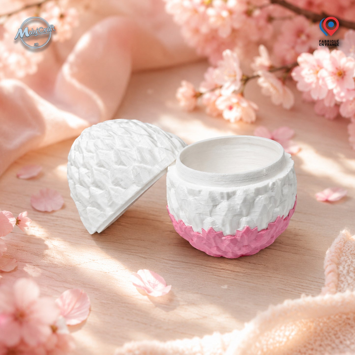 Œuf de dragon articulé blanc et rose cherry blossom, impression 3D artisanale MalyCraft3D, posé sur bois clair entouré de fleurs de cerisier et tissu rose poudré, ambiance printanière douce et lumineuse. Création Cinderwings